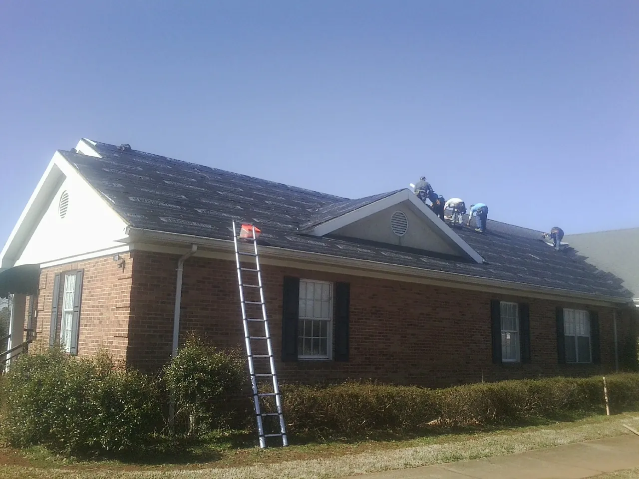 Crew tearing shingles off a brick ranch roof with a ladder set — Emergency Roof Repair work by our crew in Cabot