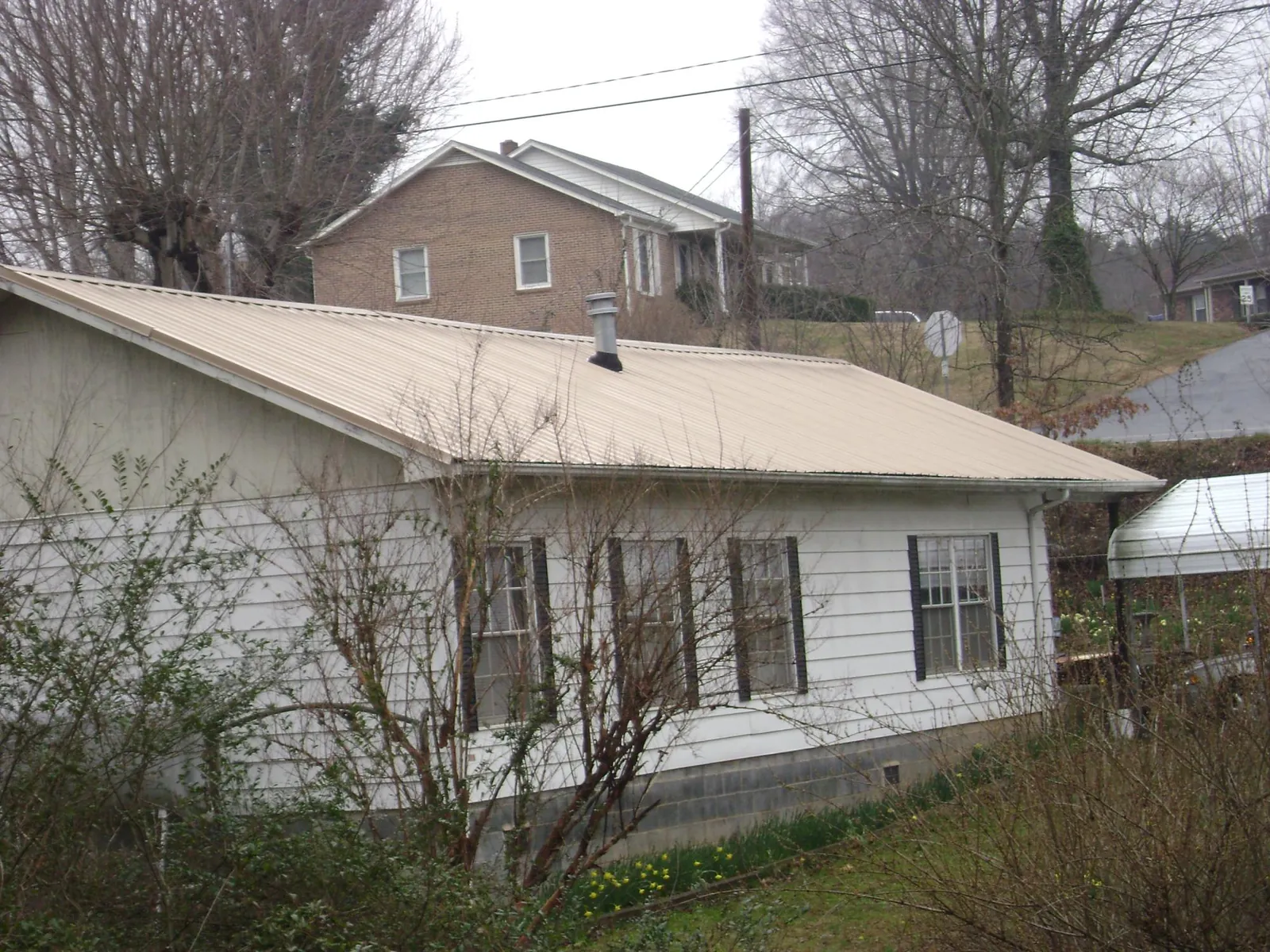 Tan metal roof on a white sided house set into a hillside — Commercial Roofing by Roofing Brothers in Cabot